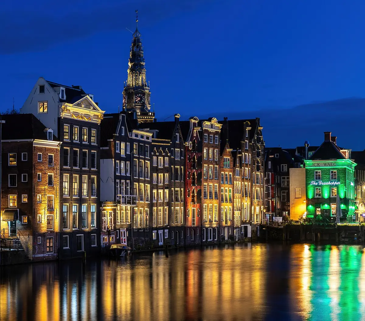 Canal houses and Oude Kerk at blue hour with water reflection in Damrak Amsterdam Netherlands